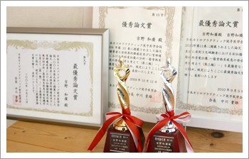 学会で受賞した優秀論文賞・最優秀論文賞の賞状とトロフィー