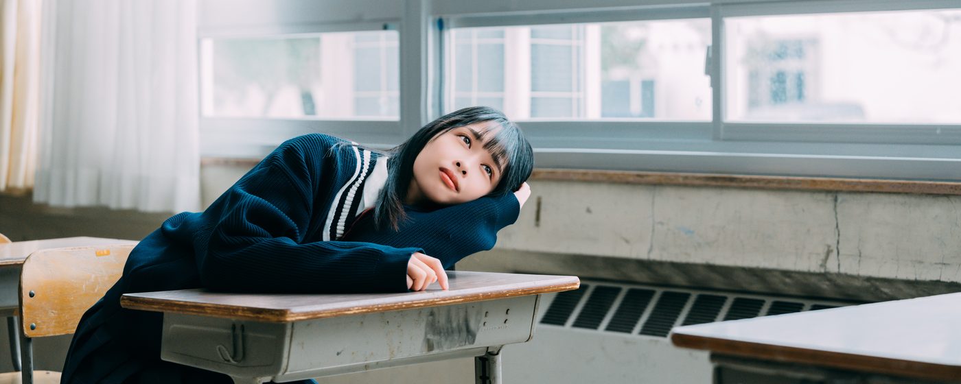 教室の机に伏せる制服姿の学生（イメージ）